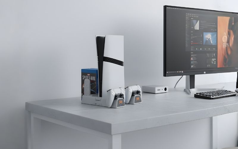 Stanowisko z konsolą PS5 w podstawce YAXO Arctic Breeze NE oraz dwoma kontrolerami ustawione na biurku obok monitora