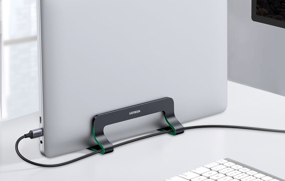 MacBook w podstawce UGREEN z podłączonymi kablami na białym biurku